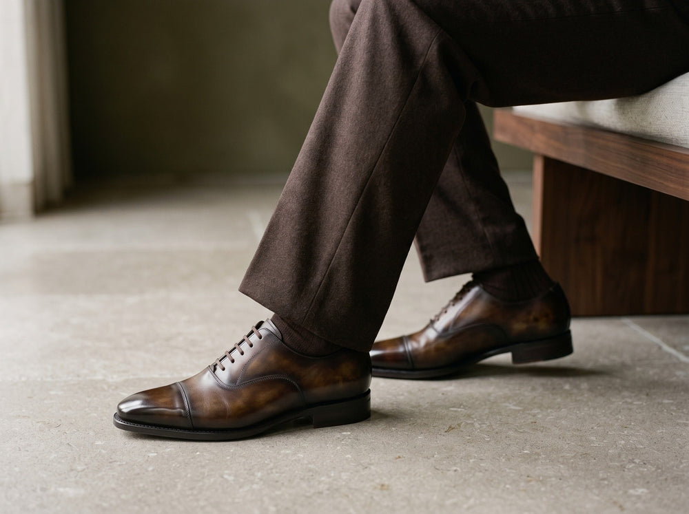 Tobacco patina Oxford shoes worn with brown tailored trousers beside a wooden bench