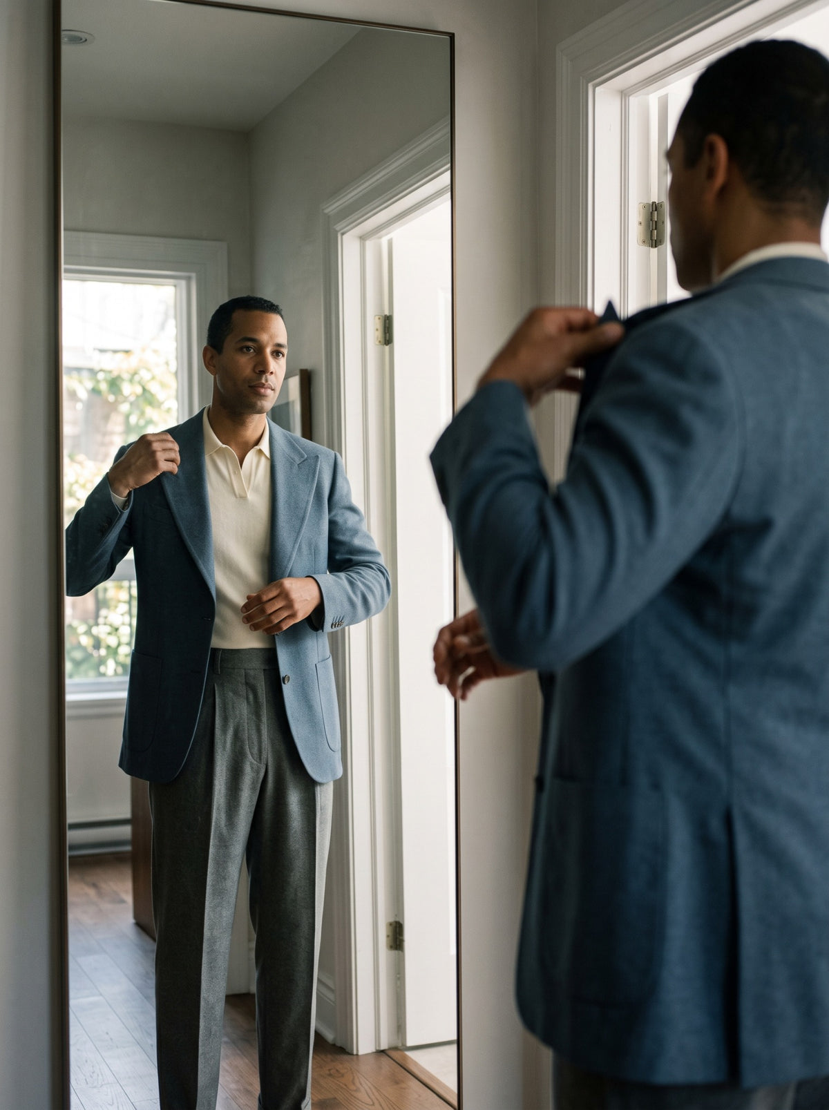 A man putting on a blue wool jacket beside a mirror