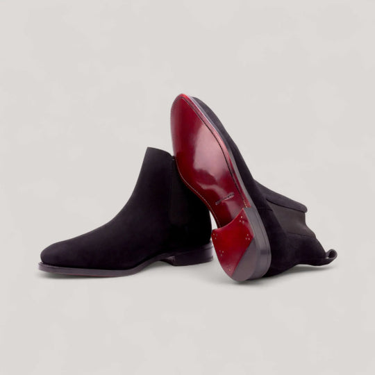 Black suede Chelsea boots showing the burgundy leather sole