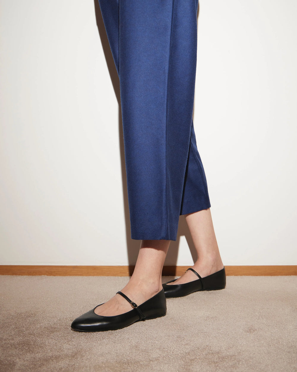 Woman wearing cropped blue trousers and black leather Mary Jane flats on carpet
