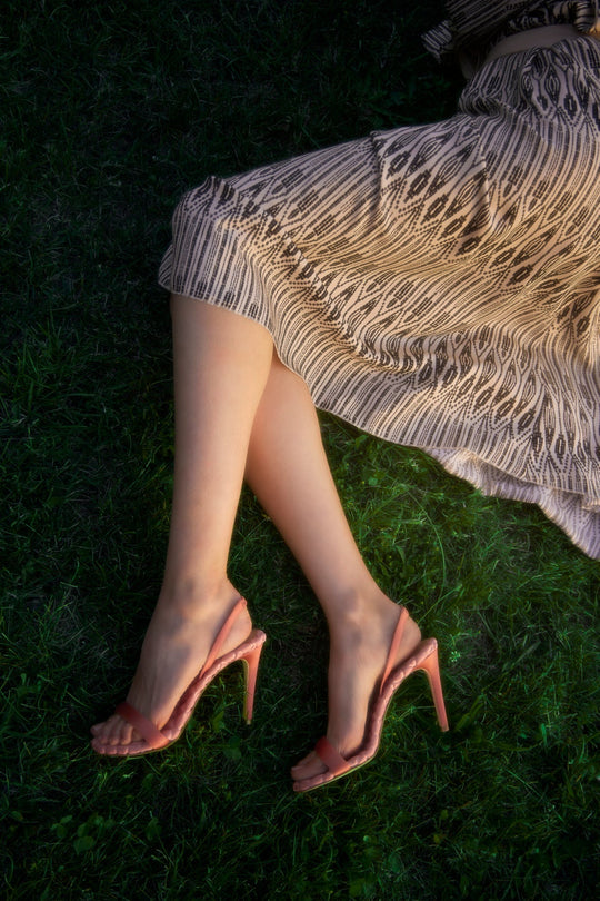 Model wearing AERA VIVIEN antique rose slingback sandals with a pleated skirt on grass.