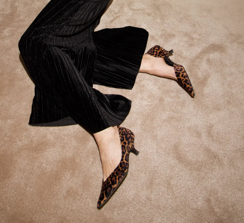 Woman wearing black pleated pants and leopard print kitten heel shoes on beige carpet
