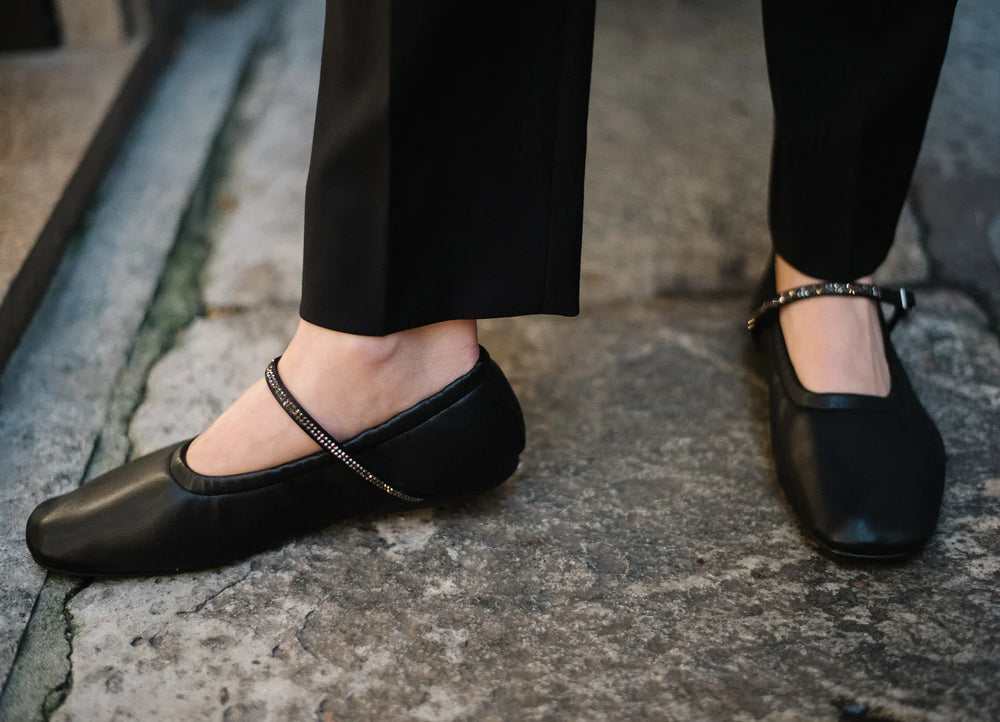 Woman wearing AERA Aurora black Nappa Crystal Mary Jane flats, vegan and sustainable shoes, on stone pavement.