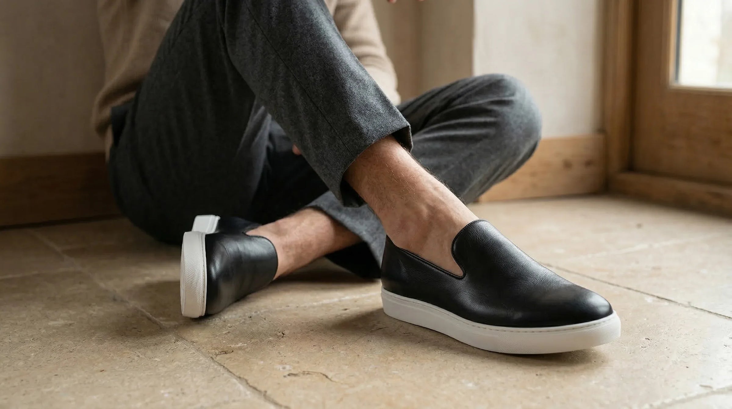 Black leather loafers with white soles worn by a person in grey pants on a stone floor