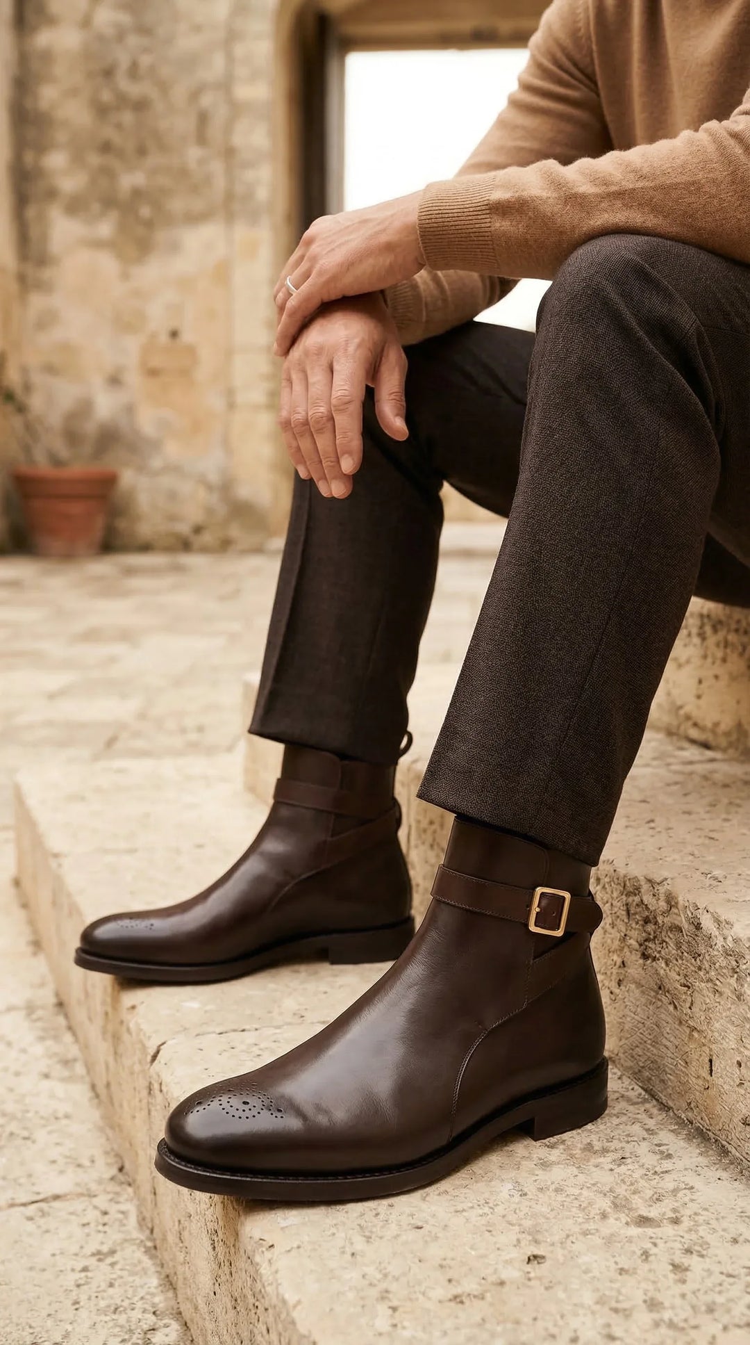 Man wearing brown leather Jodhpur boots with buckle detail and brogue toe, seated on stone steps