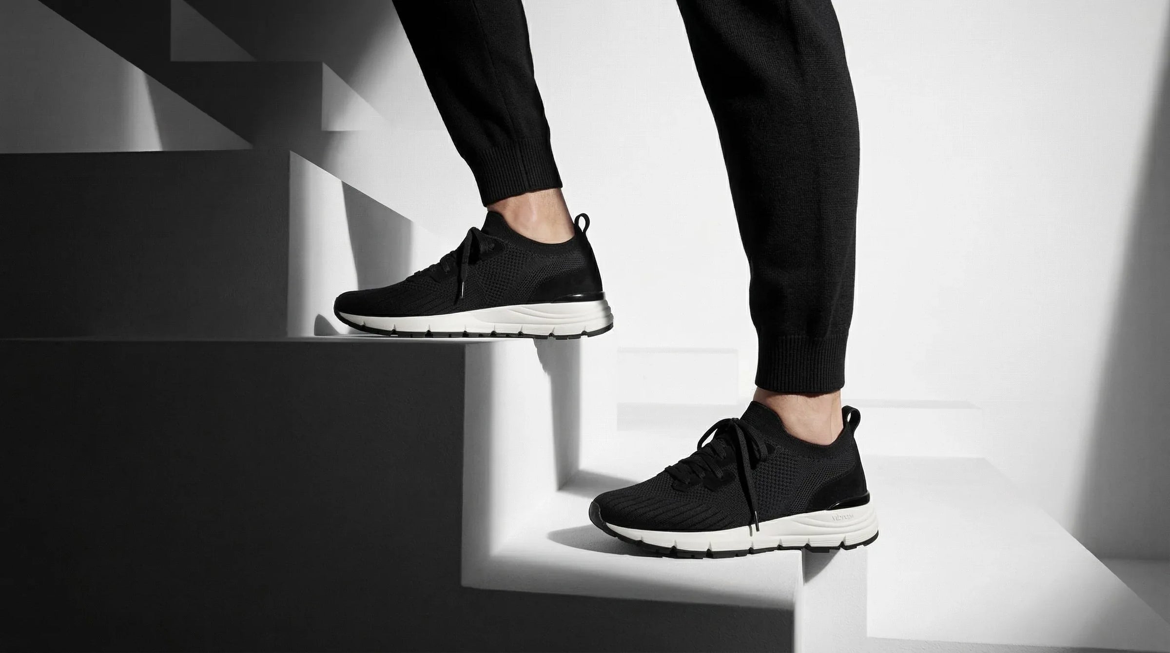 Black knitted sneakers with white soles worn on stairs, modern minimalist setting