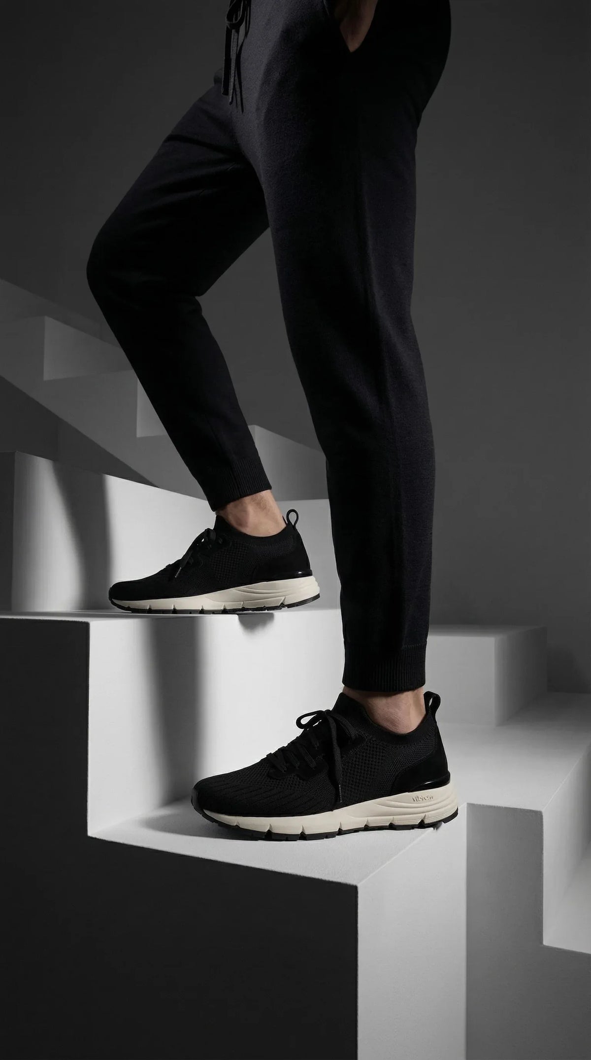 Black knitted sneakers with white soles on a person standing on modern geometric stairs
