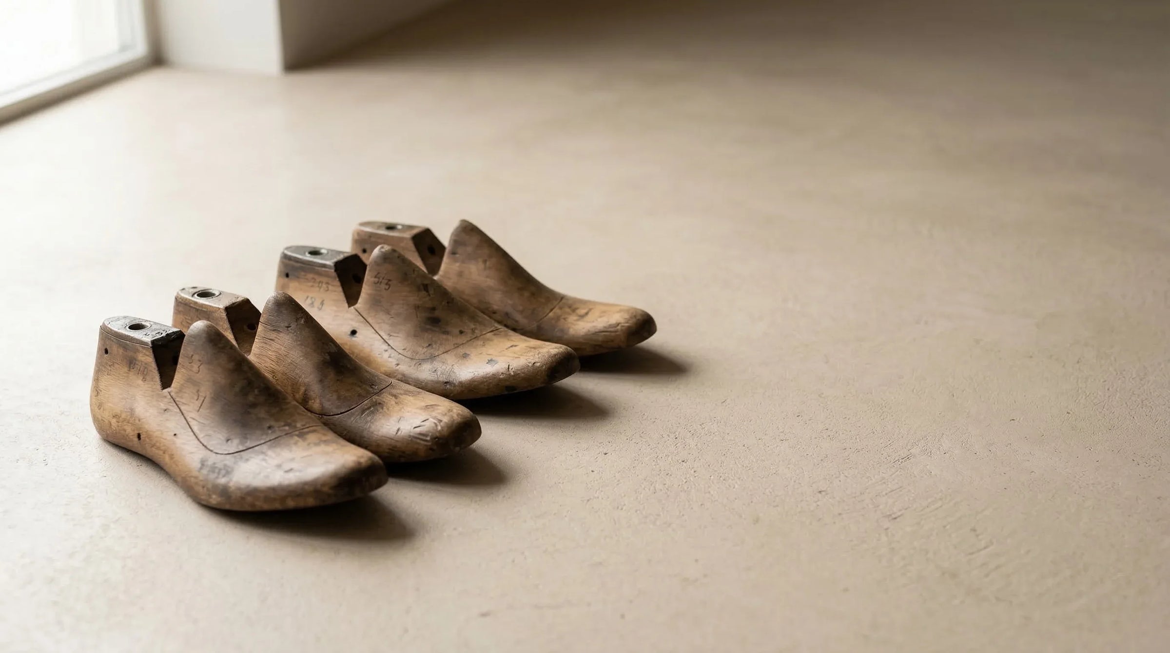 Four wooden shoe lasts lined up on a light beige floor in natural light