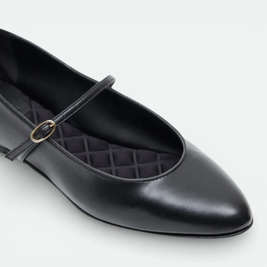 Black leather Mary Jane flat shoe with gold buckle and quilted insole on white background