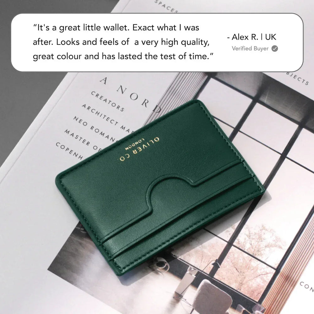 Slim green leather card holder with gold embossing on a magazine, minimal modern style.
