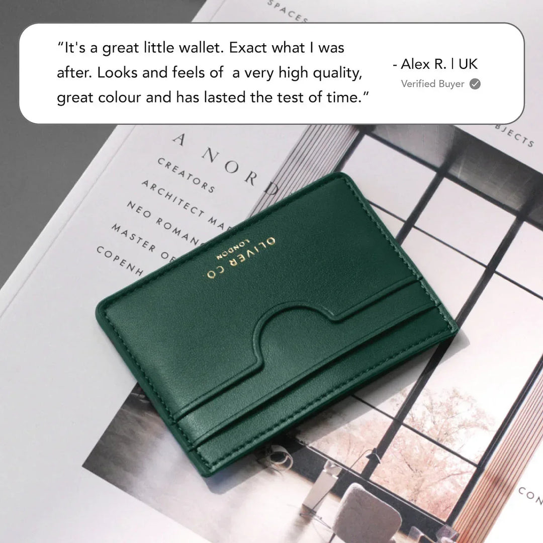 Slim green leather card holder with gold embossing on a magazine, minimal modern style.