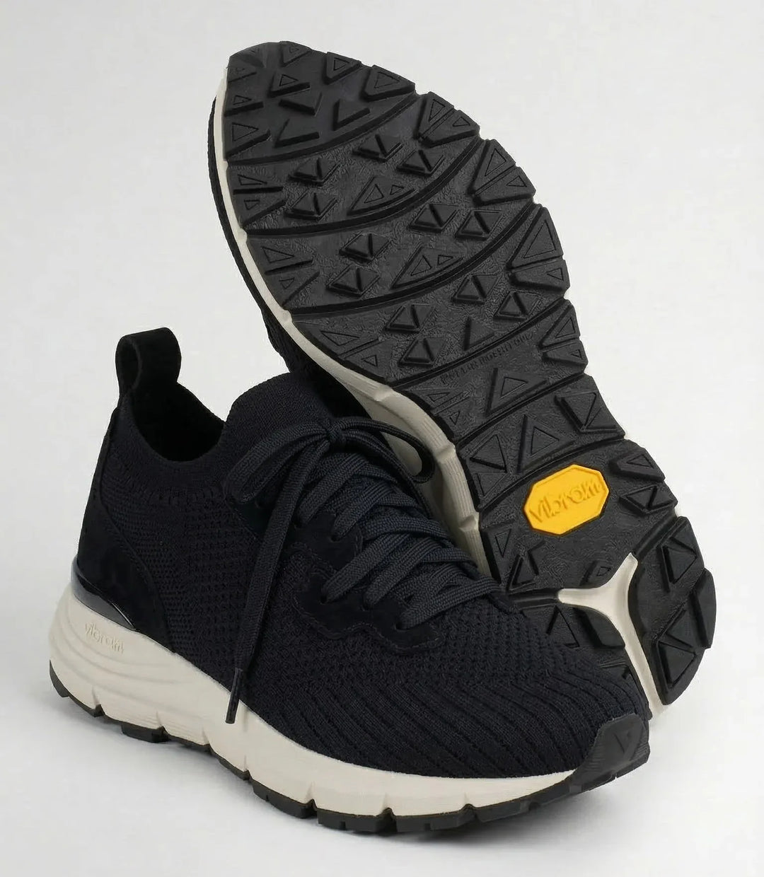 Black knit sneaker with white sole and textured black Vibram outsole, front and bottom view