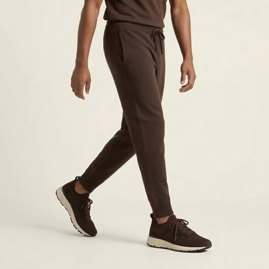 Man wearing brown suede jogger pants and dark knit sneakers on neutral background
