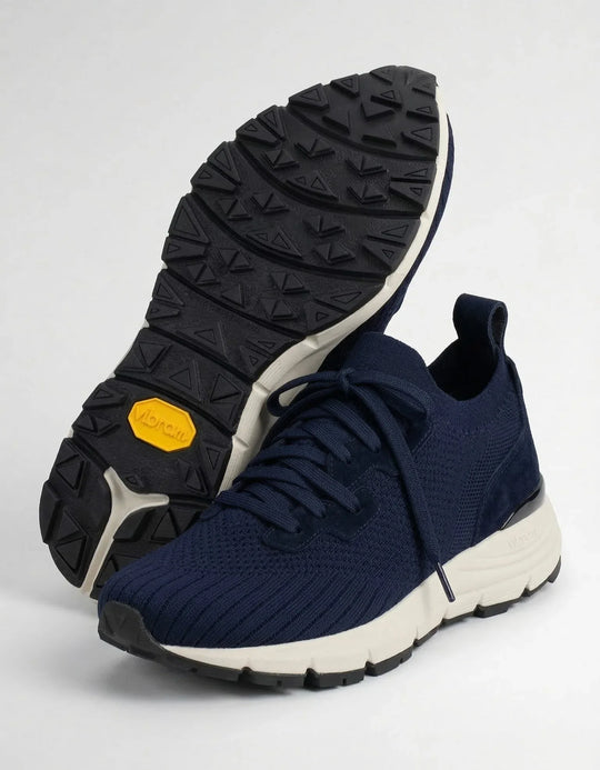 Navy blue knit sneakers with white soles and black Vibram outsoles on a white background.