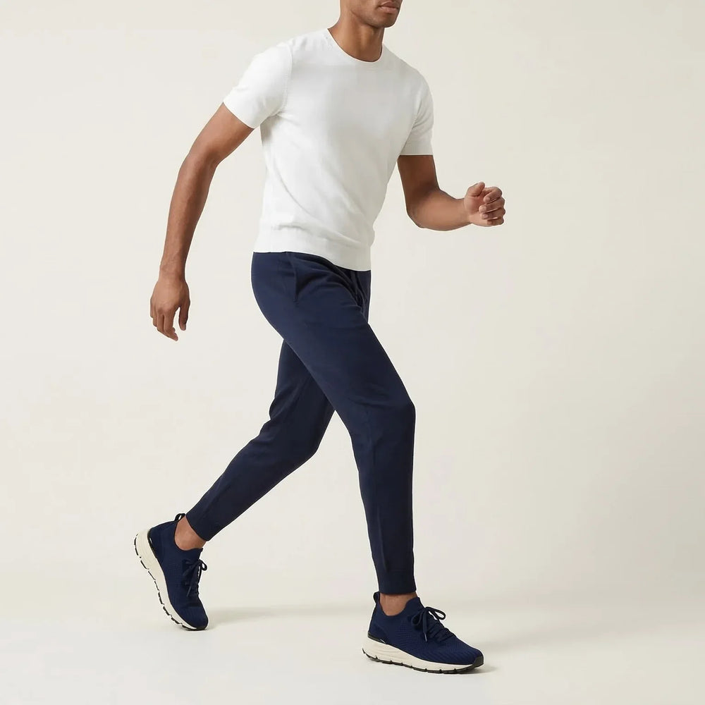 Man wearing navy blue suede sneakers, navy joggers, and white t-shirt walking indoors