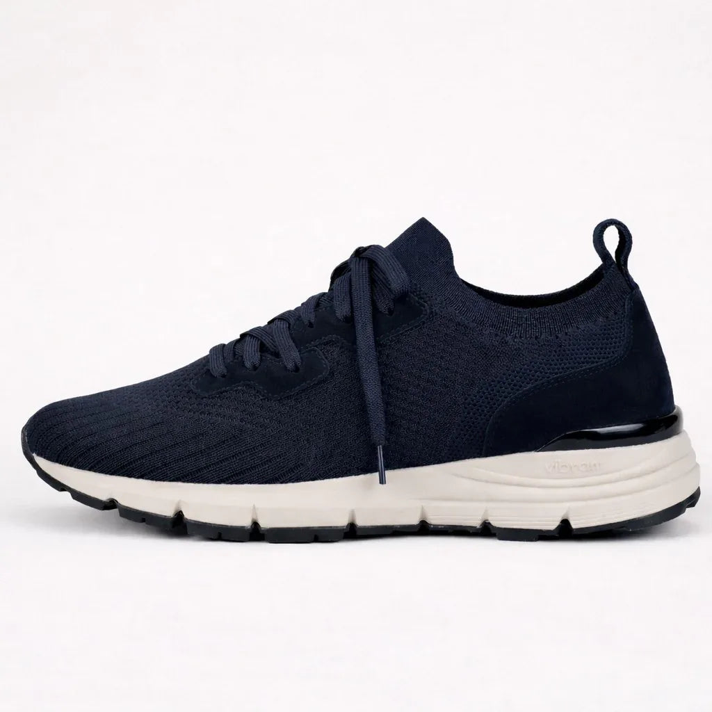 Navy blue suede knit sneaker with white sole and lace-up design on plain background