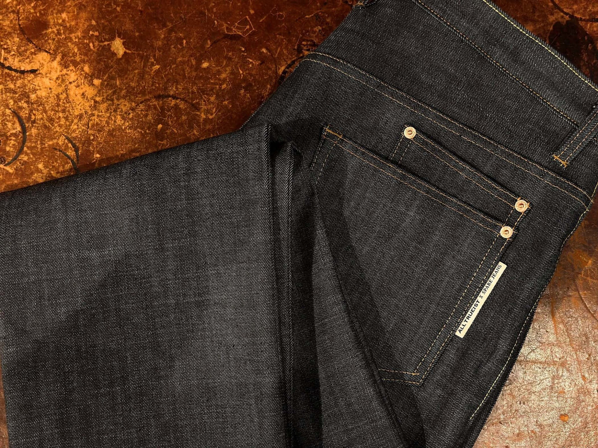 Close-up of dark Japanese denim jeans with contrast pocket stitching, brass rivets and the Alltrueist × Spare Jeans label