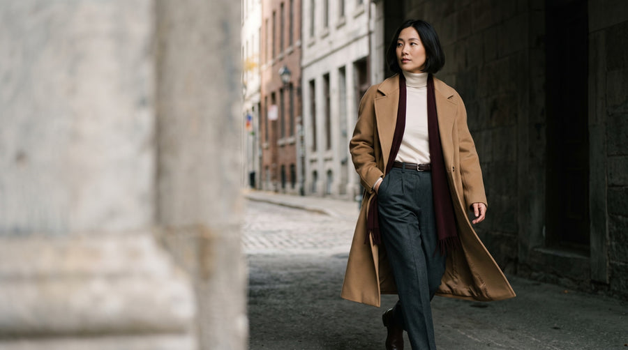 A woman in a camel coat beside a stone passage in Old Montréal
