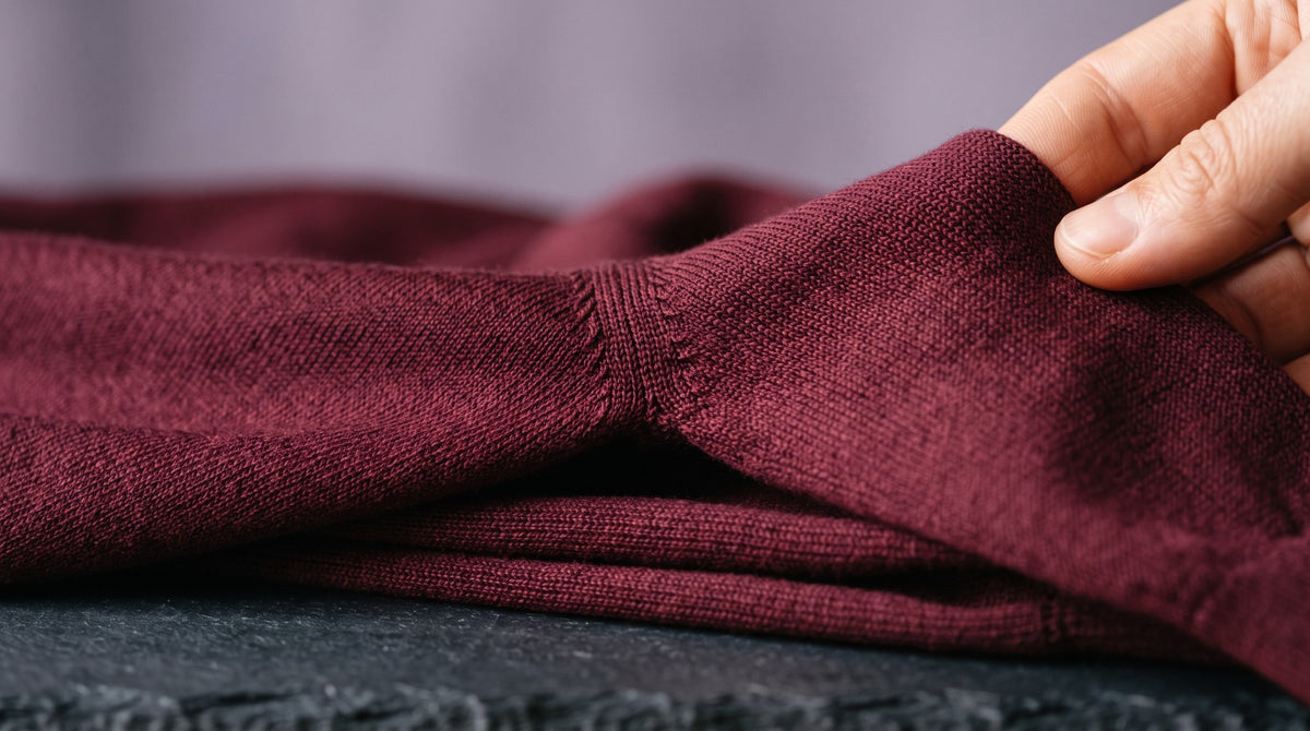 Close view of the fine stitches and sleeve shaping of a burgundy knit garment.