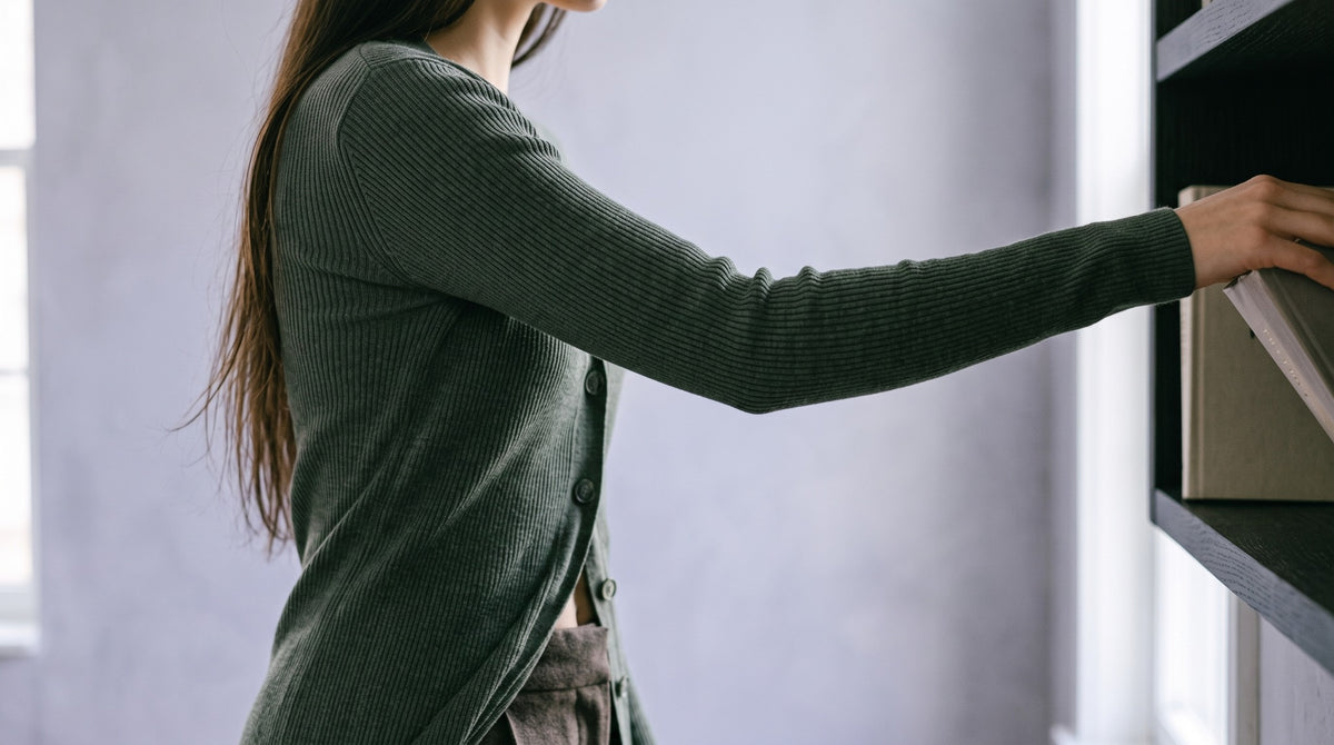 Woman reaching towards a shelf in a green fine-knit sweater.