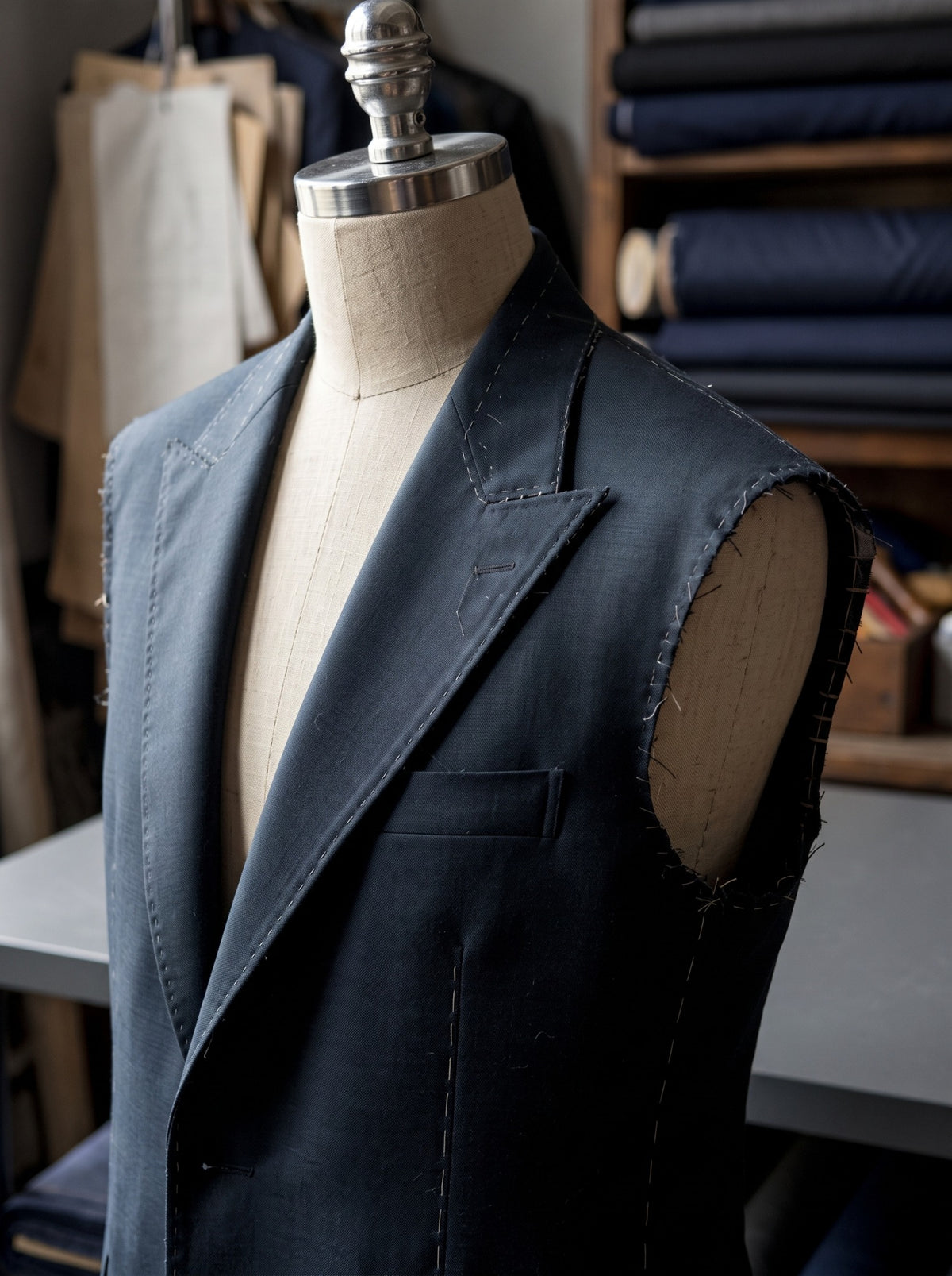 An unfinished navy jacket with temporary basting and open armholes on a tailoring form