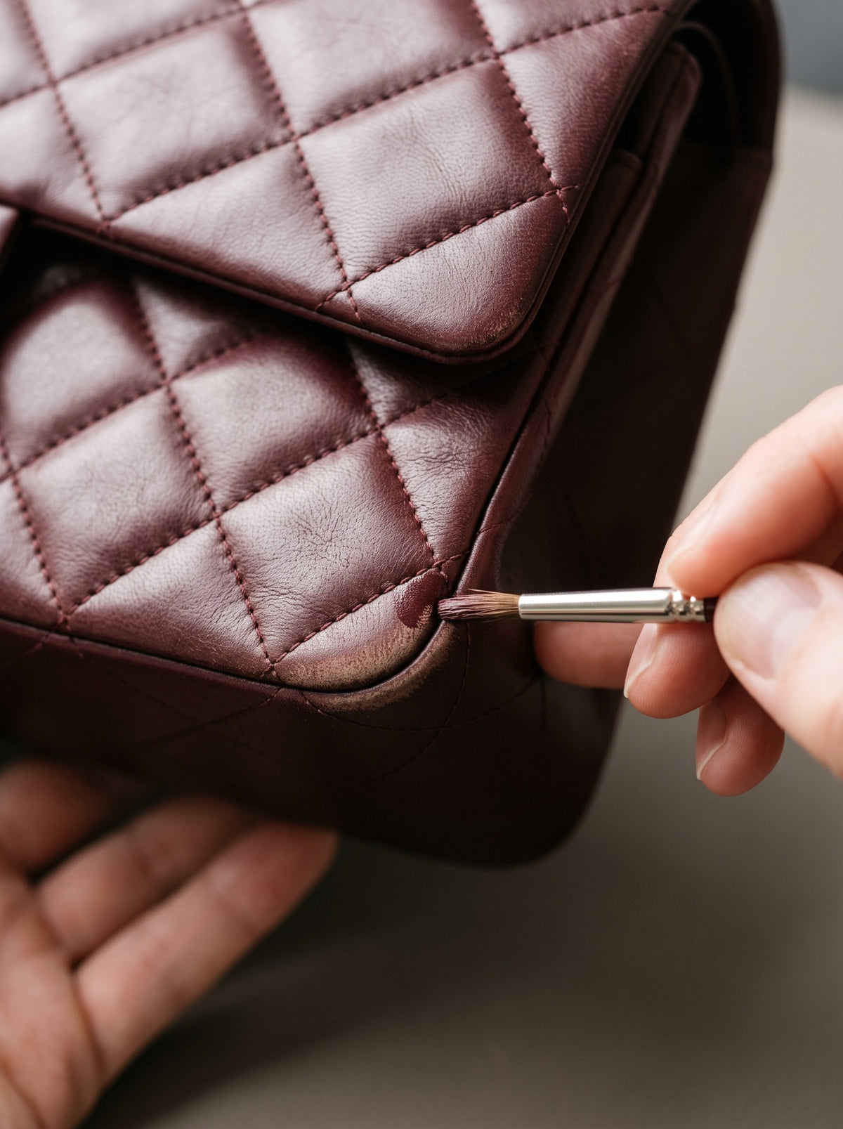 A specialist restoring colour to the worn corner of a burgundy quilted handbag