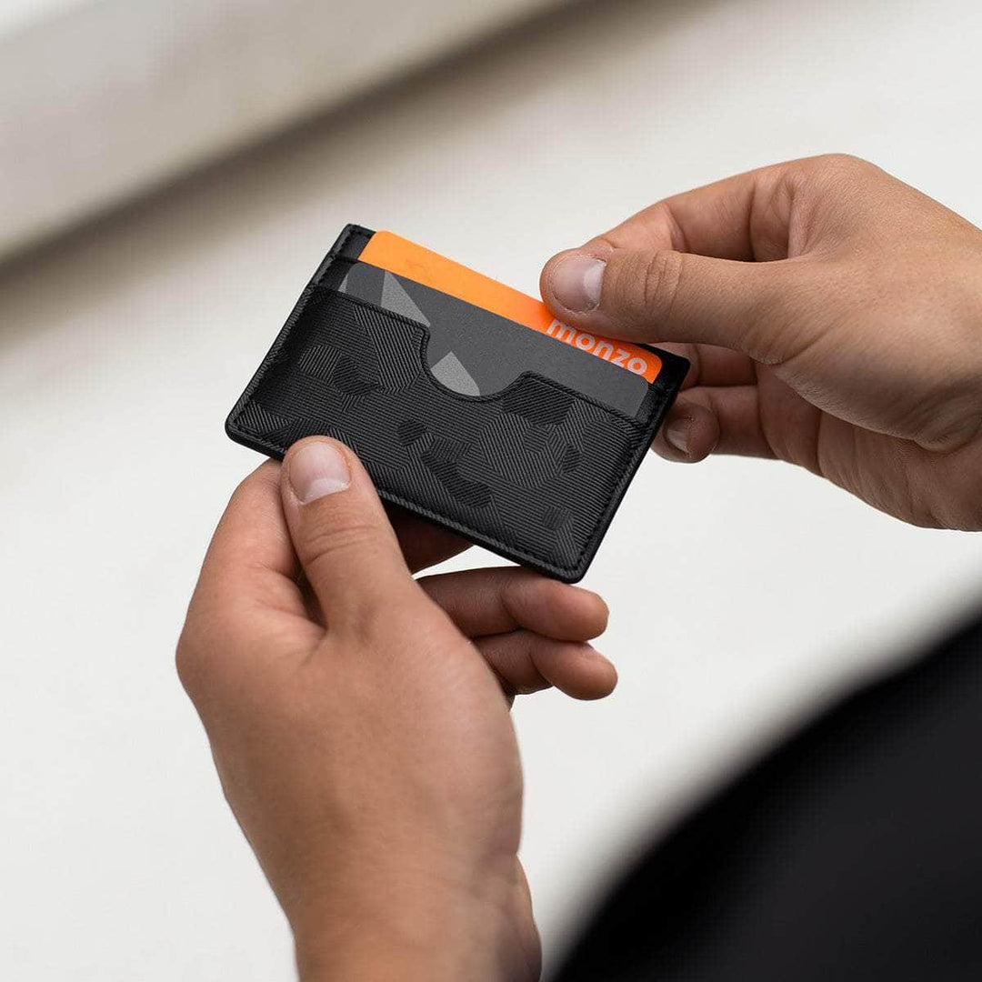 Hands holding a black vegan leather slim card holder with geometric pattern and credit cards.