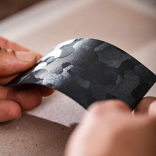 Hands holding a slim, black vegan card holder with a textured, patterned finish