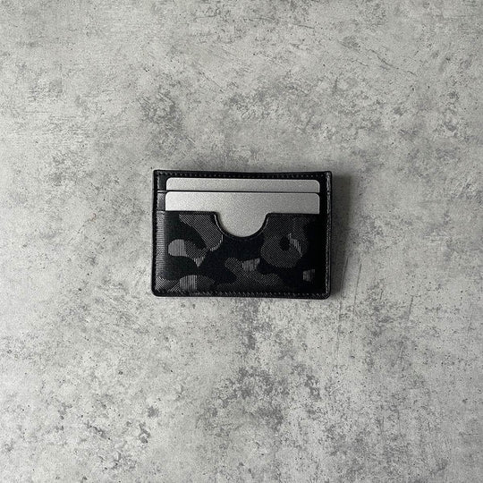 Black vegan slim card holder with camo pattern, holding two silver cards on a gray surface
