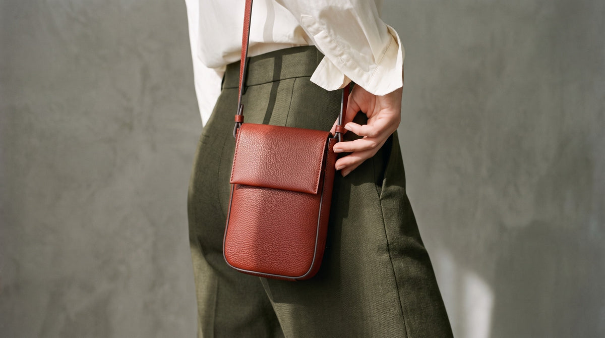 Woman carrying a terracotta Two.B crossbody bag with olive trousers and an ivory shirt.